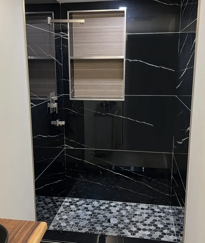 A finished shower with black marble-look tile and a hex mosaic floor